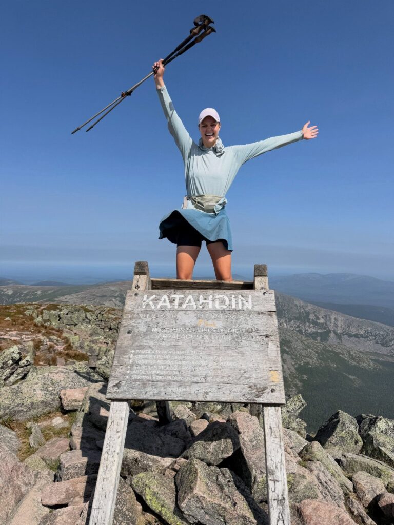 Woman celebrating on top of the Katahdin sign at a rocky mountain summit