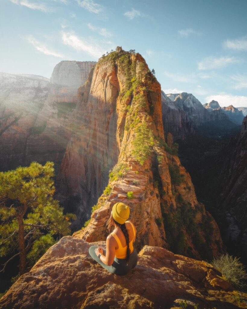 Woman sitting on a rocky ledge overlooking steep red sandstone cliffs in Zion Canyon.