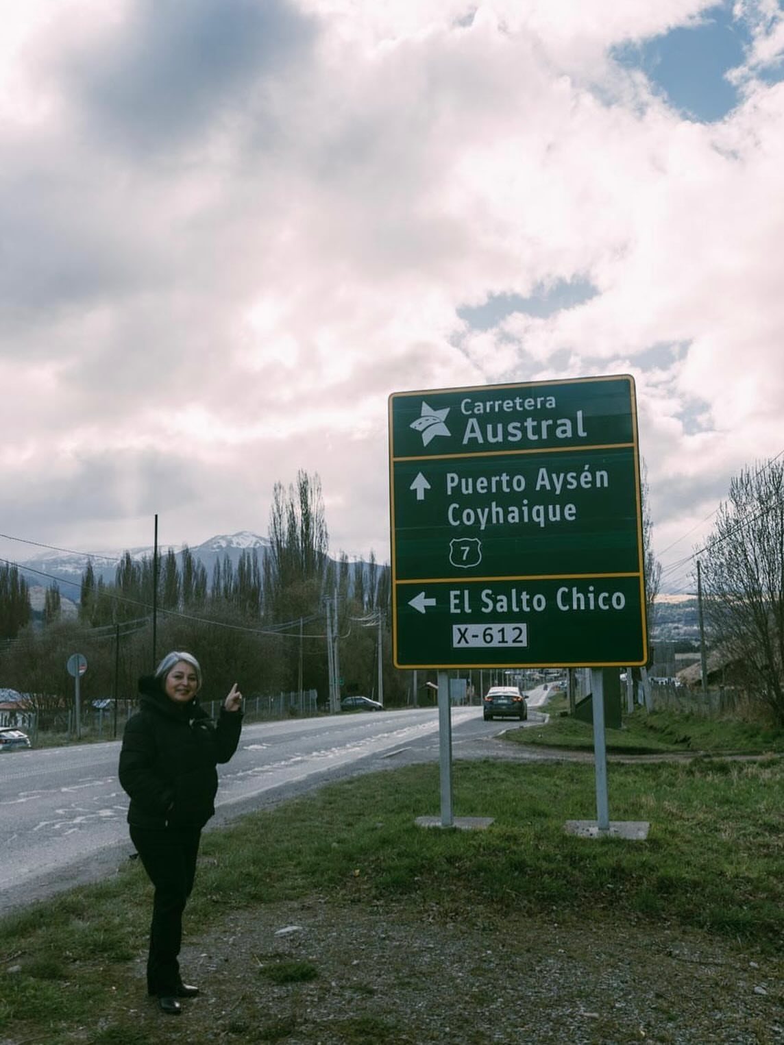 Woman standing next to a Carretera Austral road sign with mountains in background