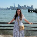Woman in polka dot dress posing before the New York City skyline and waterfront.
