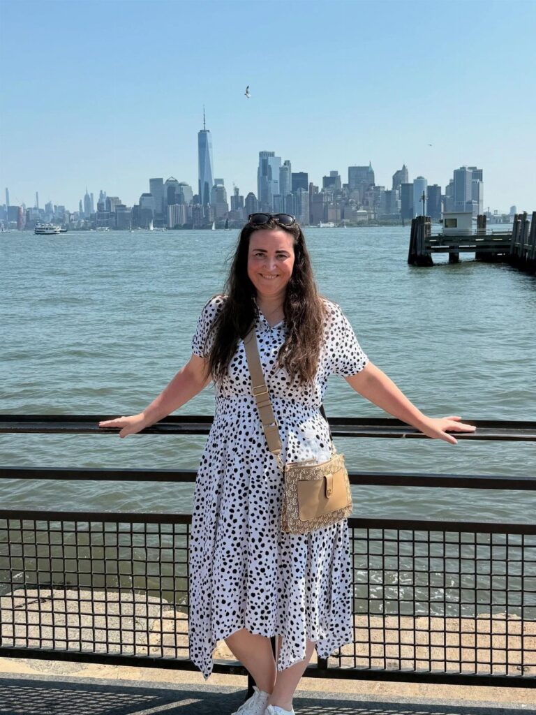 Woman in polka dot dress posing before the New York City skyline and waterfront.