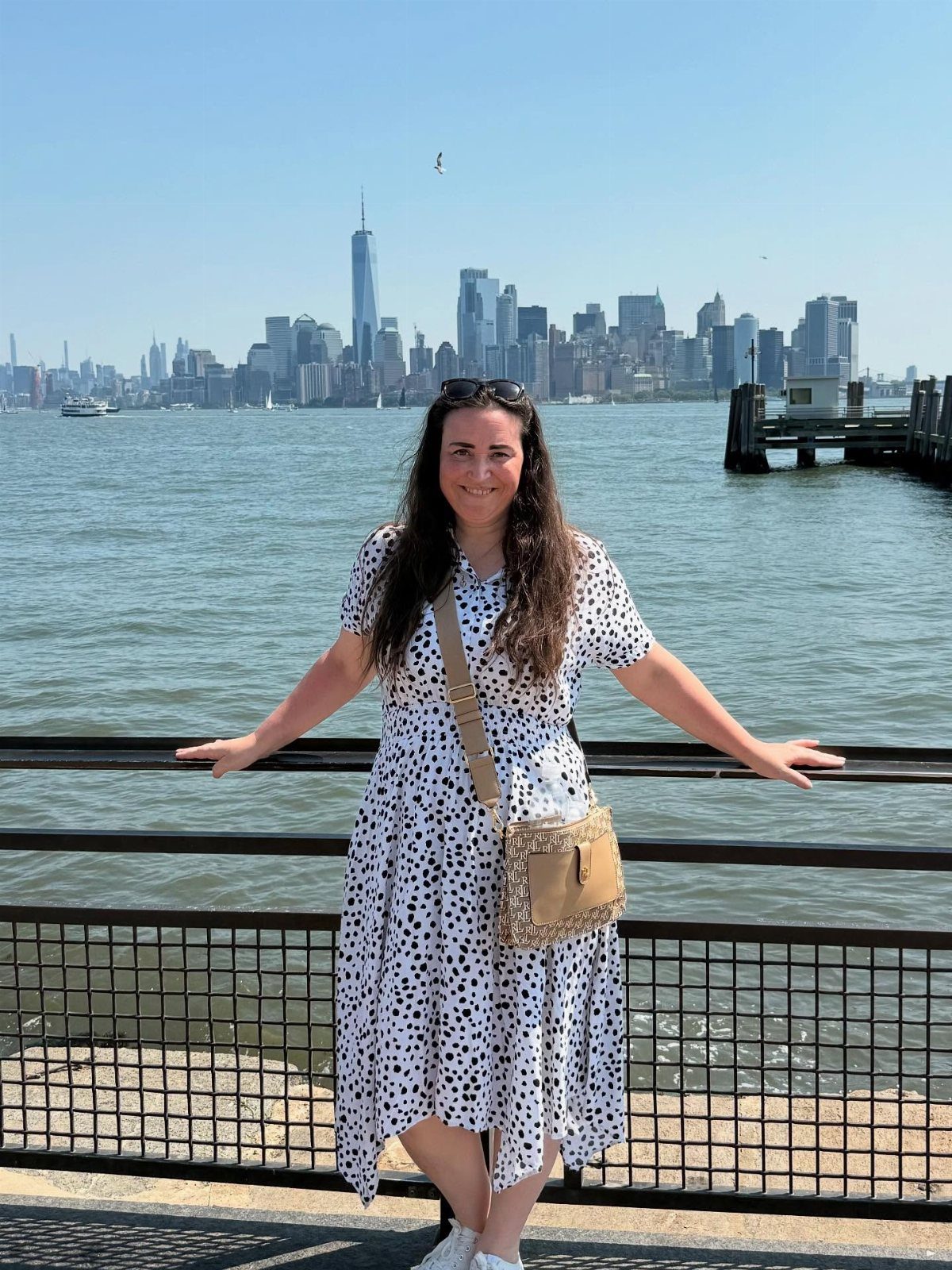 Woman in polka dot dress posing before the New York City skyline and waterfront.