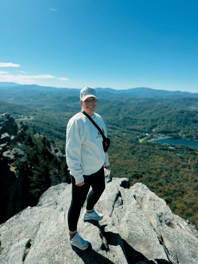 Woman standing on a rocky mountain peak overlooking autumn forests and a lake.