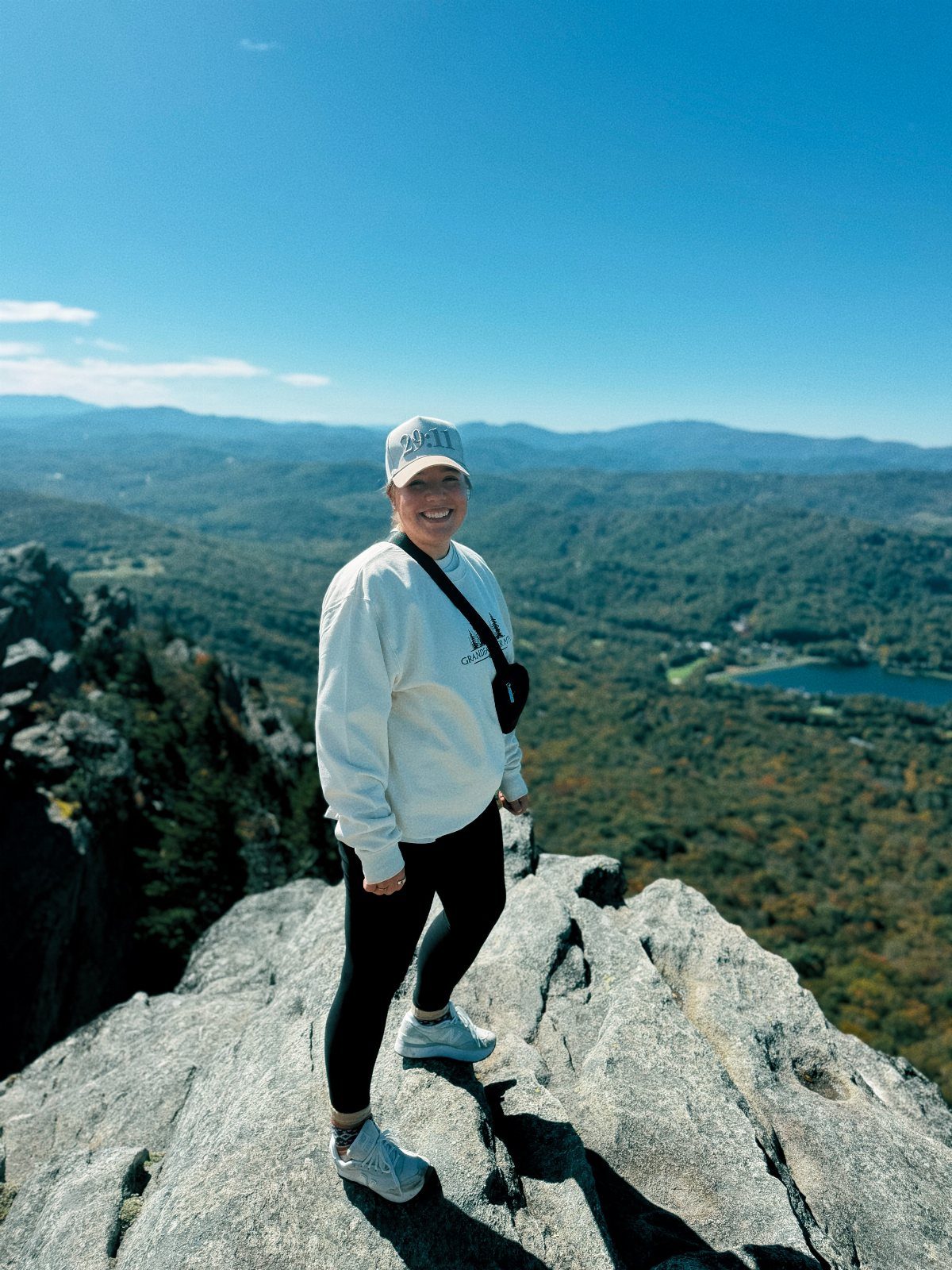 Woman standing on a rocky mountain peak overlooking autumn forests and a lake.