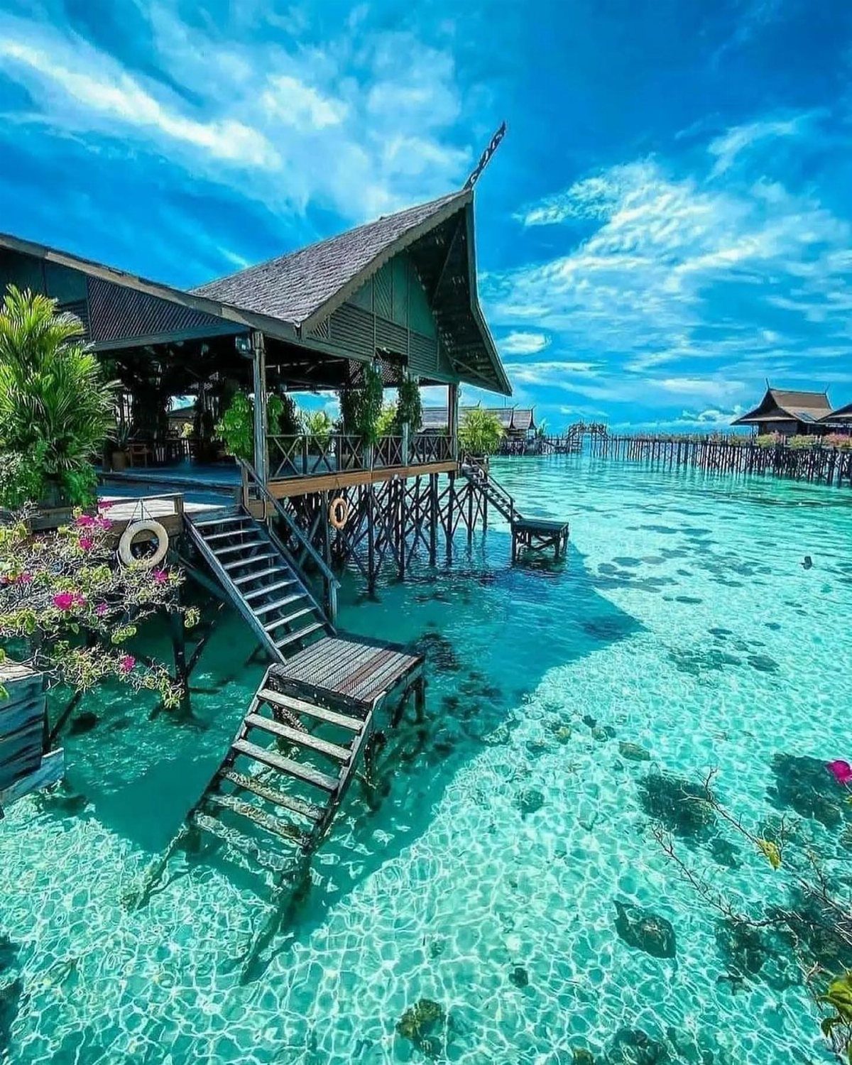 Wooden overwater villas with stairs descending into clear turquoise tropical ocean water.