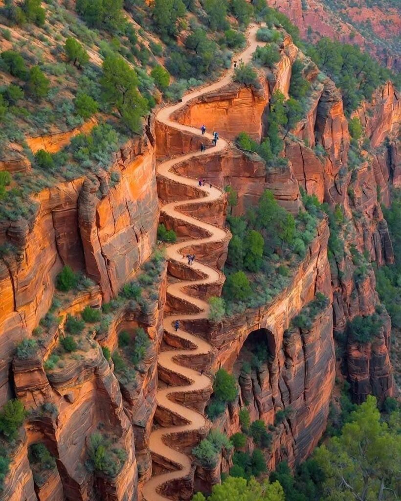 Winding hiking trail carved into steep orange sandstone cliffs with green vegetation.