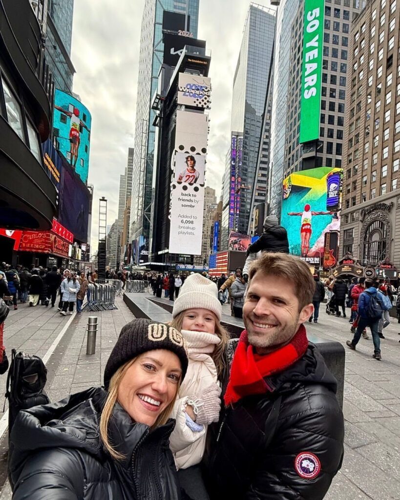 Family of three smiling for a selfie in bustling Times Square, New York City.