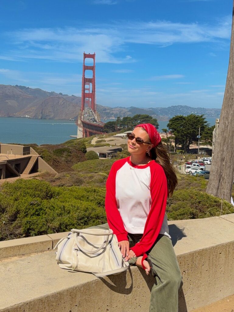 Woman in red and white shirt sitting before the Golden Gate Bridge in San Francisco