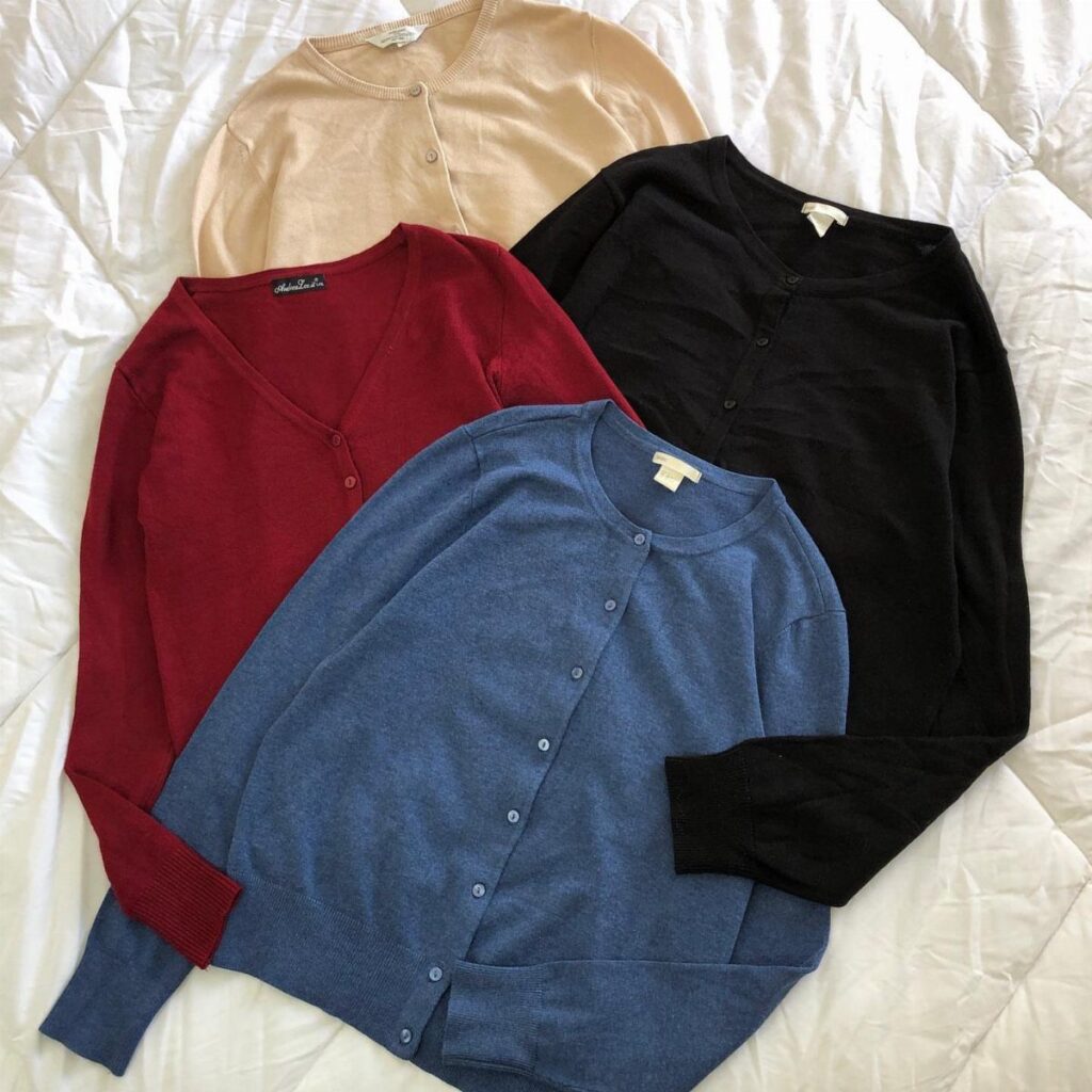 Three button-up cardigans in beige, red, and blue on a white quilted background.