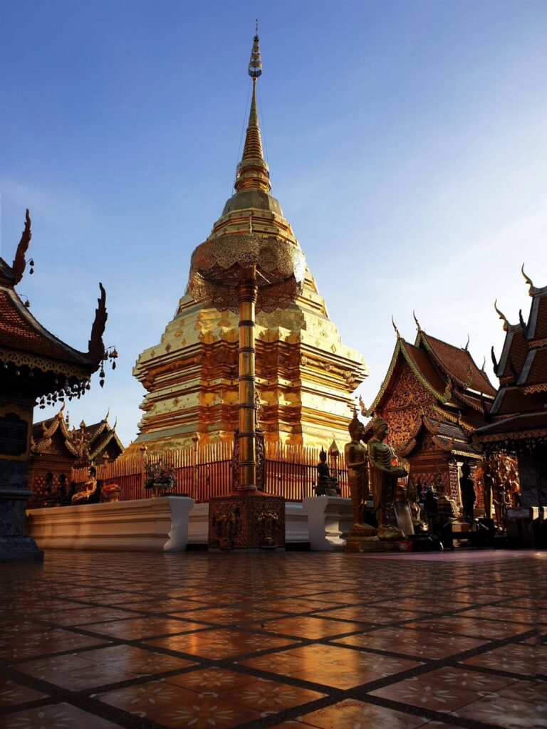 Golden bell-shaped pagoda and ornate Thai temple buildings under a clear blue sky.