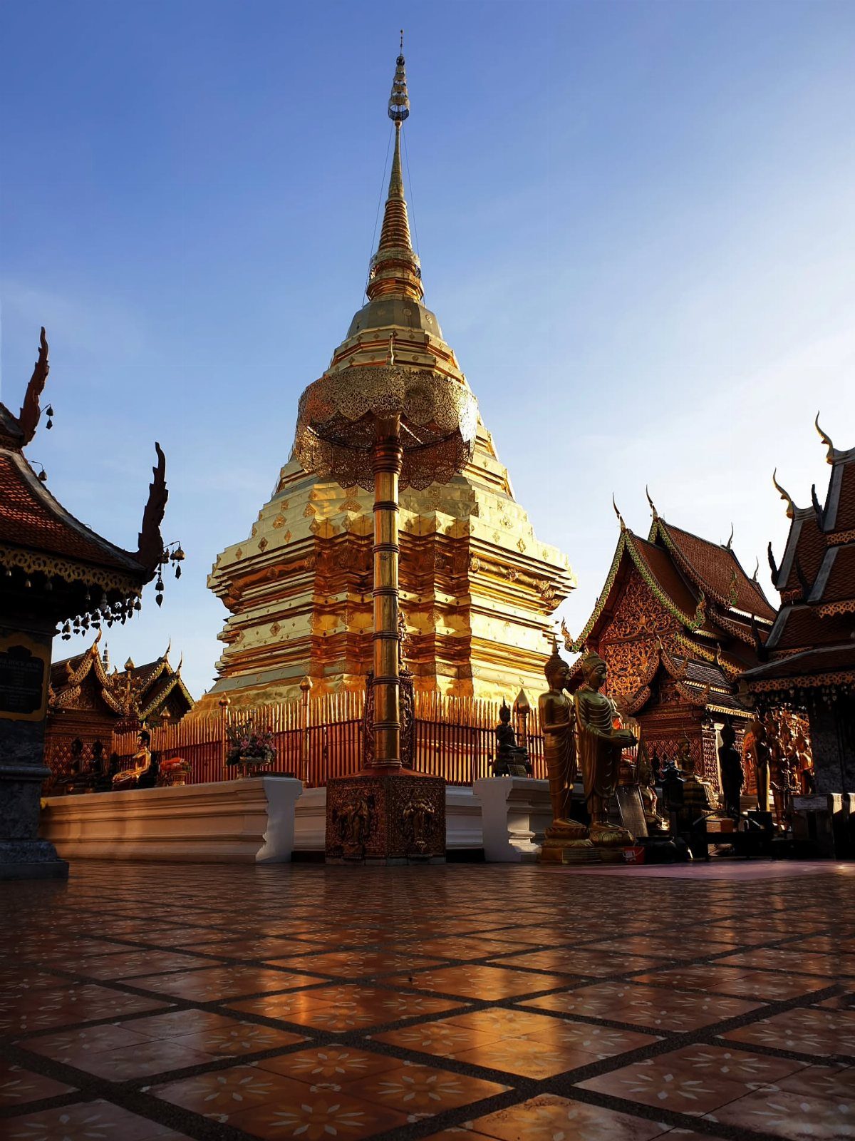 Golden bell-shaped pagoda and ornate Thai temple buildings under a clear blue sky.