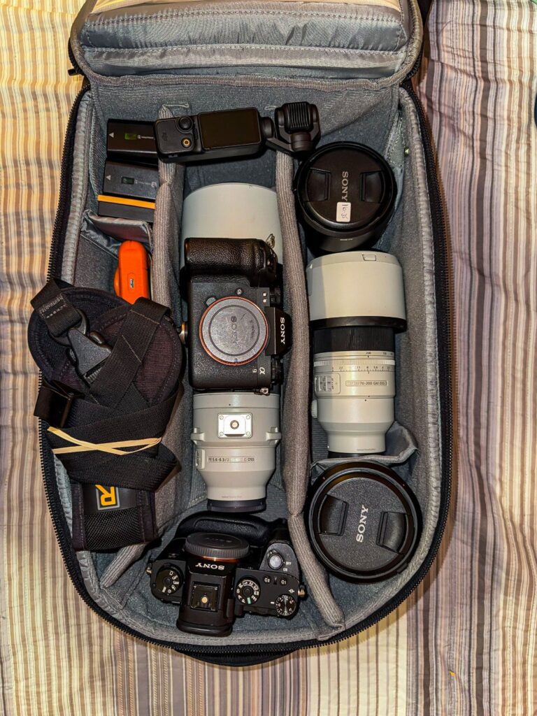 Camera equipment including Sony cameras and white lenses inside a grey padded bag.