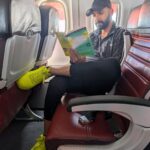 Man in yellow sneakers reading a book while sitting in an airplane seat.
