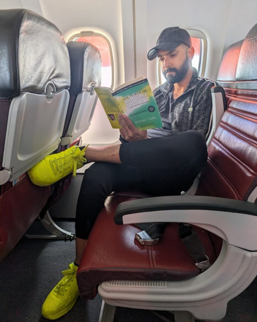 Man in yellow sneakers reading a book while sitting in an airplane seat.
